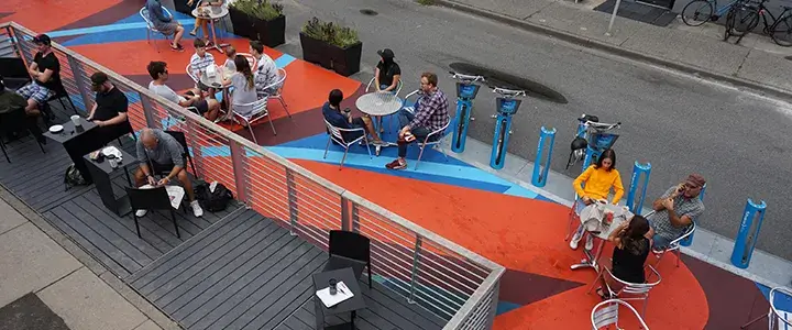 Main & 14th Plaza. Featuring a painted street mural, bike docks, planter barriers, and outdoor seating.